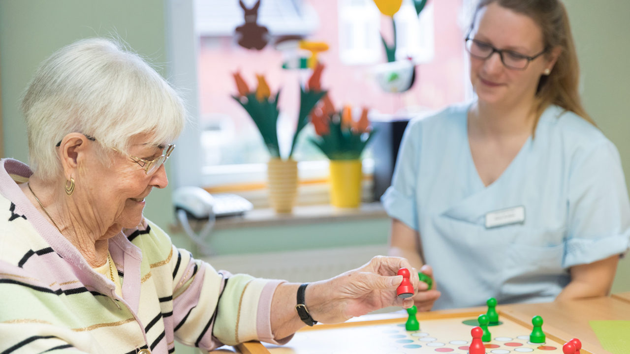 Eine Oma spielt mit einer Pflegerin ein Brettspiel im Eine ältere Frau lacht mit einer Pflegerin im Pflegeheim Seniorenresidenz Uelzen